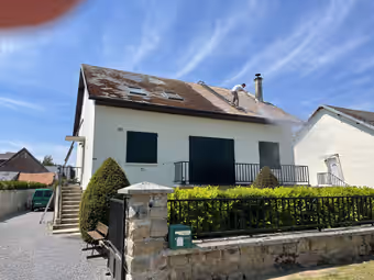 Couvreur nettoyant une toiture au jet haute pression sur une maison individuelle